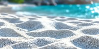 Close-up view of white sand dunes with soft texture and blurred turquoise water background creating tranquil beach atmosphere for summer vacation concept.