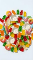 Colorful assorted gummy candies including bears, worms, rings and strips scattered on white background. Sweet treats for confectionery and dessert concepts.