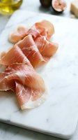 Thin slices of cured prosciutto arranged on a marble board with figs and olive oil, elegant charcuterie presentation for food blogs and menus.