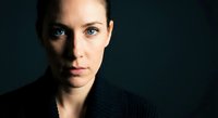 Professional portrait of confident young Caucasian businesswoman with intense gaze against dark background for corporate branding and marketing materials.