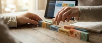 Business professional using smartphone with digital marketing icons floating above wooden desk surface for online strategy planning.
