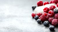 Fresh ripe raspberries and blueberries scattered on light gray concrete background with copy space, selective focus on berries in natural light.