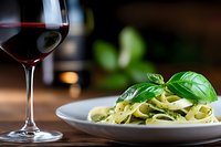 Elegant pasta dish with fresh basil and glass of red wine on wooden table in upscale restaurant setting for fine dining and culinary presentations.