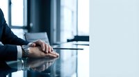 Professional businessman hands folded on conference table in modern office boardroom during corporate meeting or negotiation session.