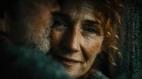 Elderly Caucasian woman with weathered face and piercing blue eyes gazing through rain-streaked window, expressing wisdom and life experience in moody lighting.