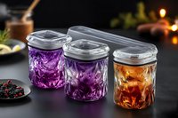 Homemade fermented vegetables in glass jars with transparent lids on dark background, purple cabbage and carrot preservation for healthy eating.