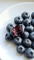 Fresh ripe blueberries in white bowl with one berry cut open showing juicy interior, healthy organic superfood for breakfast and cooking recipes.