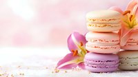 Delicate French macarons in pastel colors stacked with fresh lily flowers on pink background, soft focus composition for bakery and confectionery marketing.