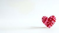 Red woven heart shape made from paper strips on white background with copy space for Valentine's Day romantic greeting cards and love messages.