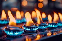 Glowing blue gas flames from multiple burners create atmospheric lighting with orange bokeh effect in dark background, close-up macro photography.