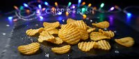 Golden ridged potato chips scattered on dark surface with colorful bokeh lights creating festive snack food atmosphere for party celebrations.