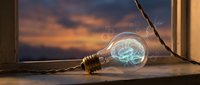 Glowing light bulb with blue plasma filament on windowsill at sunset, symbolizing innovation, creativity, and energy for design and technology projects.