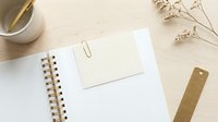 Minimalist flat lay with spiral notebook, blank note card, gold paper clip, bookmark, dried flowers on light wood desk.