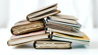Stack of old worn books and notebooks piled on a white surface, soft light background, education and knowledge concept.