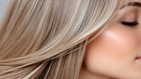 Close up profile of young woman with flowing ash blonde hair, closed eyes and natural makeup showing smooth skin texture and hair styling details.