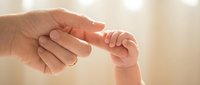 Tender moment as adult hand gently holds tiny newborn baby fingers in soft warm light creating intimate bonding scene for family and parenting concepts.