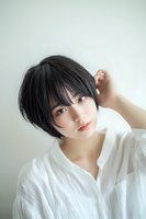 Young Asian woman with short black hair and natural makeup wearing white blouse poses against light background in soft daylight for beauty and fashion content.