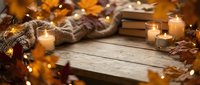 Cozy autumn scene with candles, books, knitted sweater and fall leaves on rustic wooden table with warm fairy lights creating hygge atmosphere for relaxation.