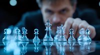 Dramatic chess composition with glass pieces on reflective surface in blue tones, player contemplating strategic move in dark background.