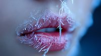Sensual red lips covered in delicate frost crystals creating an artistic winter beauty effect against dark background. Close up macro photography shows intricate ice patterns.