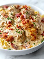 Creamy chicken and bacon pasta bake with melted cheese and fresh herbs in white casserole dish ready to serve for comfort food dinner.