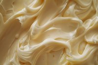 Creamy vanilla frosting texture with soft swirls and waves creating luxurious food background pattern in warm ivory and beige tones. For dessert and baking designs.