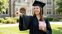 Happy female graduate in cap and gown holding piggy bank pointing finger at university campus. Education savings and student loan concept for financial planning.