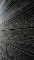 Dark weathered wood siding with horizontal planks showing natural grain texture and rustic character for architectural and construction projects.