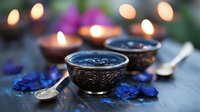 Aromatic spa composition with burning candles, ornate metal bowls, blue flower petals and spoons on dark surface, creating peaceful ambiance for relaxation.
