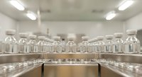 Modern pharmaceutical manufacturing facility with glass vials on stainless steel conveyor belt in sterile cleanroom environment for drug production.