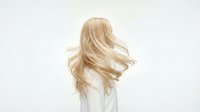 Young Caucasian woman with long flowing blonde hair tossing head, wearing white, isolated on white background. Hair care and beauty concept.