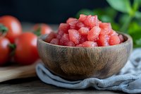 Fresh juicy watermelon cubes in wooden bowl on rustic table with tomatoes and herbs. Natural lighting creates appetizing mood for healthy summer food.