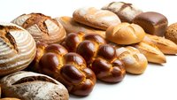 Assorted fresh baked bread loaves and rolls including sourdough, baguettes, and braided challah arranged on white background for bakery display.