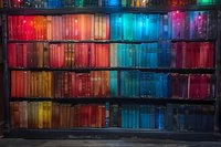 Colorful bookshelf with books arranged by spectrum from red to blue, illuminated by vibrant lighting creating a rainbow effect in a library or bookstore.