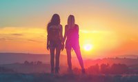 Two female silhouettes standing together against vibrant sunset sky over mountain landscape, creating atmospheric mood with golden light and dreamy gradient colors.