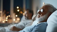 Senior Caucasian man with white beard relaxing in bed wearing sleep mask, bokeh lights in background creating peaceful nighttime atmosphere.