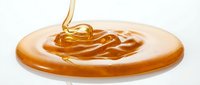 Golden honey drips onto wooden plate, creating swirls of liquid sweetness. Perfect for food, culinary, and organic product marketing materials.