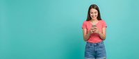 Young woman using smartphone on turquoise background. Casual brunette female in coral top and jeans texting, browsing social media for lifestyle content.