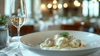 Homemade potato gnocchi in creamy sauce garnished with fresh herbs and parmesan, served with white wine in elegant restaurant setting with bokeh lights.