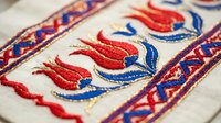 Traditional folk embroidery with red and blue floral motifs on white fabric. Handcrafted textile art featuring decorative border patterns for cultural projects.
