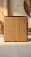 Closed corrugated cardboard box with kraft paper exterior and black tape sealing edges, positioned on white surface with warm natural lighting and blurred background for packaging, shipping, storage and delivery concepts.