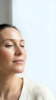 Serene middle-aged Caucasian woman with natural makeup looking away thoughtfully in soft natural light wearing cream sweater for wellness and beauty content.