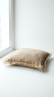 Rustic burlap throw pillow with fringe edges placed near a bright window, showcasing natural jute texture and boho home decor style.