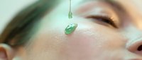 Young woman receiving green serum facial treatment with dropper for skincare routine and anti-aging therapy in spa wellness center.