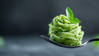 Fresh pesto pasta twirled on fork with basil leaf garnish against dark background for culinary and food photography projects.