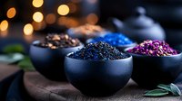 Colorful dried flowers and tea leaves in black ceramic bowls on dark wooden surface with bokeh lights background, moody food photography styling.
