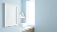 Minimalist bathroom interior with blank white frame on light blue wall, shelf with vase, folded towels on marble countertop near window.