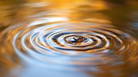 Mesmerizing concentric water ripples with golden sunset reflections creating hypnotic circular patterns on calm water surface, abstract nature background.