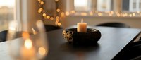 Cozy home interior with burning candle in decorative bowl on dark table, warm bokeh lights creating peaceful ambiance for relaxation and meditation.