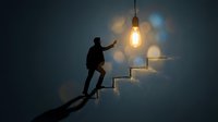 Business professional climbing illuminated staircase toward glowing lightbulb representing career growth, success and achievement in corporate environment.
